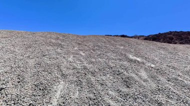 Geniş ve kayalık bir arazi, canlı mavi bir gökyüzü altında, doğanın saf güzelliğini gözler önüne seriyor.