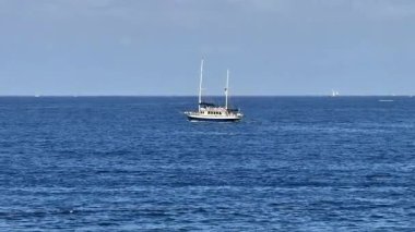 Güzel, resimsi bir yat, berrak mavi gökyüzünün altındaki sakin okyanus sularında zarifçe yüzüyor.
