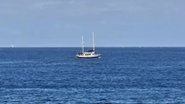 Görkemli ve lüks bir yat berrak mavi gökyüzünün altında sakin okyanus sularında pürüzsüzce süzülüyor.