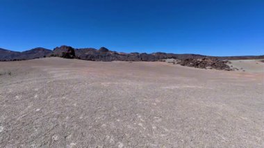 Uçsuz bucaksız bir çöl manzarası, engin ve berrak bir gökyüzünün altında kayalık dağların oluşturduğu çorak bir araziyi gözler önüne seriyor.