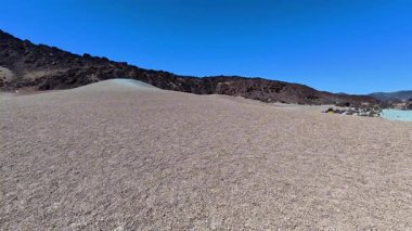 Göz kamaştırıcı bir çöl manzarası keşfedin. Kıvrımlı kumullar ve engebeli tepeler, parlak mavi bir gökyüzü altında..