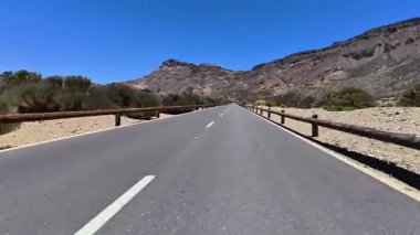 Görkemli dağların ve açık mavi gökyüzünün altında kıvrılan uzun, dolambaçlı bir yolun nefes kesici manzarasını ele alalım.