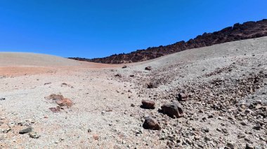 Açık mavi gökyüzüne karşı, kuru ve kayalık bir manzaranın nefes kesici görüntüsü, saf güzellikleri gözler önüne seriyor.