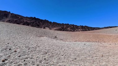 Üzerinde mavi bir gökyüzü olan kayalık bir çöl arazisinin nefes kesen manzarası doğal güzellikleri gözler önüne seriyor..