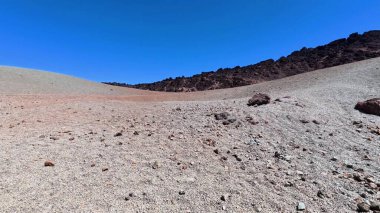 Uçsuz bucaksız ve kurak bir arazinin nefes kesici manzarası, berrak, mavi gökyüzünün altındaki engebeli kayalık araziyi gözler önüne seriyor.
