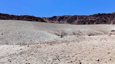 Kuru, kayalık bir manzarada yuvarlanan tepeler ve berrak mavi bir gökyüzü, doğal güzellikler sergiliyor..