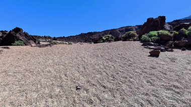 Parlak mavi gökyüzünün altındaki kayalık bir arazinin çarpıcı manzarası doğal güzellik ve sükuneti gözler önüne seriyor..