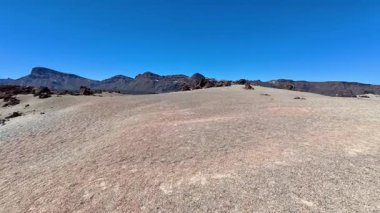 Çarpıcı bir çöl manzarası sergiliyor, canlı mavi gökyüzüne karşı kayalık tepeler sunuyor.