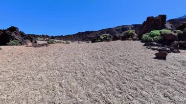 Yukarıda açık mavi bir gökyüzü altında çarpıcı bir dizi kayalık oluşumları barındıran engin ve kurak bir manzara.