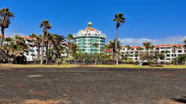 Palmiye ağaçları ve açık mavi gökyüzünün altındaki siyah kumlarla çevrili lüks bir tropikal tatil köyünün manzarası.