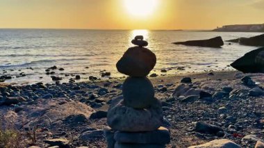 Huzurlu ve sakin bir gün batımı sahnesi kayalık bir plajda mükemmel dengelenmiş taşlar sergiliyor.