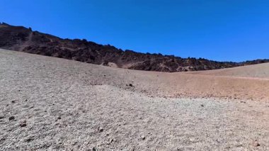 Üzerinde mavi bir gökyüzü olan kayalık bir çöl arazisinin nefes kesen manzarası doğal güzellikleri gözler önüne seriyor..