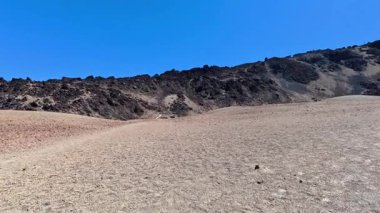 Açık mavi gökyüzünün altında eşsiz kayalık oluşumların yer aldığı geniş ve kurak bir arazinin nefes kesici manzarasını deneyimleyin.