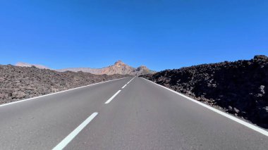 Büyüleyici, dolambaçlı bir yol, berrak mavi gökyüzünün altında, katıksız, dramatik bir volkanik arazide zarifçe kıvrılır.