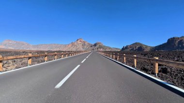 Nefes kesici bir manzara, berrak mavi gökyüzünün altında nefes kesici volkanik bir arazide dolambaçlı bir yolu gösteriyor.