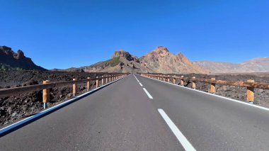 Resimli bir yol volkanik arazide dönüyor, görkemli kaya oluşumlarını ve açık gökyüzünü gösteriyor..