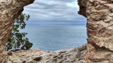 Uçsuz bucaksız okyanus manzarası engebeli bir taş kemer tarafından çerçevelenmiş, onu çevreleyen yemyeşil yemyeşil ile tamamlanmış.