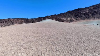 Temiz mavi gökyüzünün altında eşsiz tepe oluşumlarıyla çorak bir çöl manzarası..