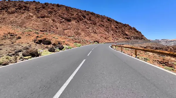 Güzel, dolambaçlı bir yol çarpıcı kayalık dağların arasından geçiyor, hepsi parlak, açık mavi gökyüzünün altında.