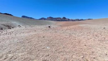 Kuru toprak ve berrak mavi gökyüzünün altındaki engebeli bir dağ zeminiyle karakterize edilen engin, kurak bir bölge.