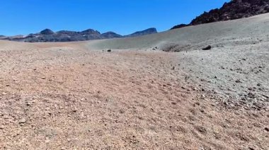 Bu çarpıcı kayalık çöl sahnesi yukarıdaki açık mavi gökyüzüne karşı canlı toprak tonlarını sergiliyor.