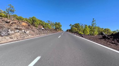 Dolambaçlı ve pitoresk bir yol geniş çapta yol alır yemyeşil ve kayalık manzaralar berrak, mavi bir gökyüzü altında.