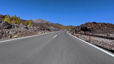Mavi gökyüzünün altında volkanik kaya ve yemyeşil ile çevrili dolambaçlı bir yol boyunca bir yolculuğa çıkın.
