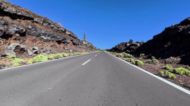 Güzel, resimli, dolambaçlı bir yol parlak mavi bir gökyüzünün altında nefes kesici volkanik bir arazide ilerliyor.
