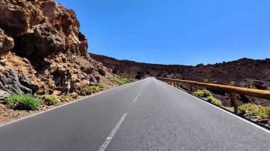 Benzersiz volkanik kaya oluşumları ve açık mavi gökyüzü ile çevrili nefes kesici bir yol keşfedin..