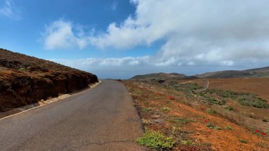 Çarpıcı bir yol kenarı manzarası engebeli araziyi ve parlak mavi gökyüzünün altında güzel manzaralı bir kıyı şeridini yakalıyor.