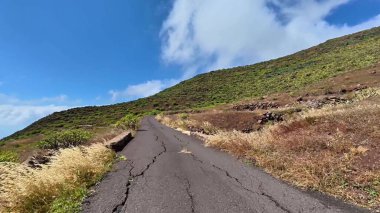 Etrafı canlı yeşilliklerle ve kabarık bulutlarla çevrili dolambaçlı bir yolun çarpıcı manzarası, keşifleri davet ediyor.