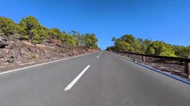 Dolambaçlı ve pitoresk bir yol geniş çapta yol alır yemyeşil ve kayalık manzaralar berrak, mavi bir gökyüzü altında.