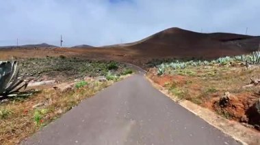 Dolambaçlı bir yol, bulutlu bir gökyüzünün altındaki görkemli dağlarla çevrili canlı, yemyeşil bir yolda zarifçe kıvrılır.