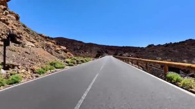 Benzersiz volkanik kaya oluşumları ve açık mavi gökyüzü ile çevrili nefes kesici bir yol keşfedin..