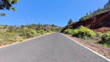 Göz kamaştırıcı dağların arasında, güneşli mavi bir gökyüzünün altında canlı yeşilliklerle çevrili güzel bir yol var.