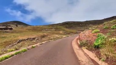 Güzel, dolambaçlı bir yol açık mavi gökyüzünün altındaki yemyeşil tepelerden ve engebeli kayalık araziden geçer.