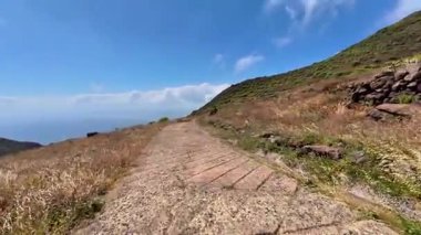 Parlak mavi bir gökyüzünün altındaki canlı tepelerin arasında dolanan dolambaçlı bir yolun nefes kesici ve çarpıcı bir görüntüsü.