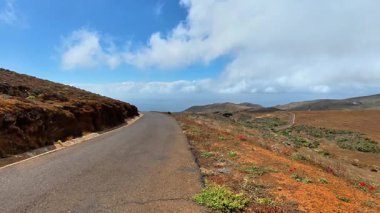 Çarpıcı bir yol kenarı manzarası engebeli araziyi ve parlak mavi gökyüzünün altında güzel manzaralı bir kıyı şeridini yakalıyor.