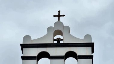 Çarpıcı bir kilise çan kulesi, zarif bir şekilde bir haç sergiliyor, karamsar, bulutlu gökyüzüne karşı güzel bir şekilde yükseliyor.