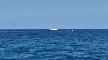 Şaşırtıcı derecede berrak mavi gökyüzüne karşı çeşitli tekne ve jet ski tasvir eden sakin ve sakin bir deniz manzarası.