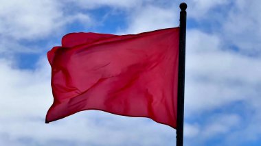 Canlı bir kırmızı bayrak, açık mavi gökyüzünün çarpıcı arka planına karşı zarif bir şekilde dalgalanır.