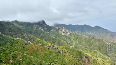 Bulutlu bir gökyüzünün altında yumuşak sislerle kaplanmış yemyeşil dağların büyüleyici manzarası.