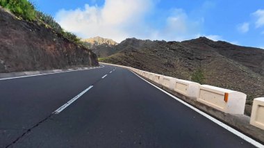 Şaşırtıcı derecede güzel, dolambaçlı bir yol, yukarıdaki parlak mavi gökyüzünün altında yemyeşil dağların arasında dolanıyor.