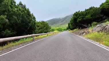 Etrafı yemyeşil ve bulutlu gökyüzünün altındaki tepelerle çevrili dolambaçlı bir yolda maceraya atılmak.