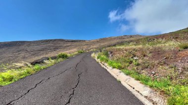 Dönek asfalt bir yol dağlık bir alana kurulmuş, canlı yeşillikler ve güzel gökyüzü sergileniyor..