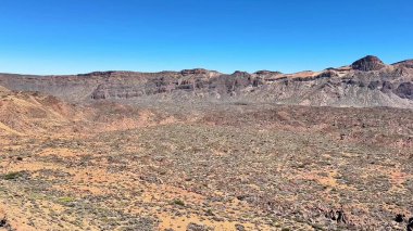 Kurak çöl arazisinin nefes kesici ve çarpıcı manzarası berrak mavi gökyüzünün altında engebeli dağlar sergiliyor.
