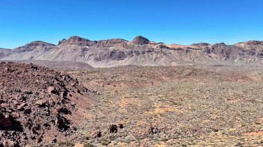 Çarpıcı bir çöl manzarası engebeli kayalık arazi ve görkemli dağ sıraları göz alıcı mavi gökyüzünün altında.
