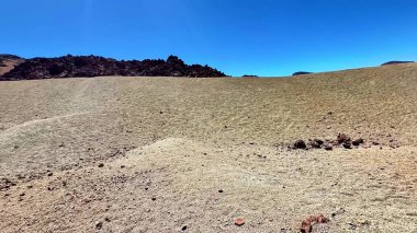 Geniş ve kurak bir arazi, temiz mavi gökyüzüne karşı kuru topraklar ve engebeli kayalık oluşumlar sergiliyor.