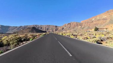 Parlak bitki örtüsü ve engebeli dağların arasından geçen dolambaçlı bir yolun çarpıcı manzarası.