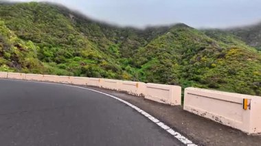 Güzel, dolambaçlı bir yol, büyüleyici bulutlu gökyüzünün altında canlı yeşil ve kayalık tepelerde zarifçe kıvrılır.